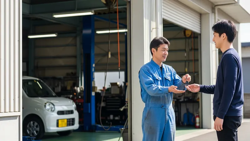 自動車整備工場の前で整備士から白い軽自動車の鍵を受け取る30代の日本人男性